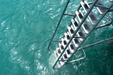 Wooden pier with ladders to the sea. Handrail. Stainless steel ladder in ocean. Grab bars ladder in...