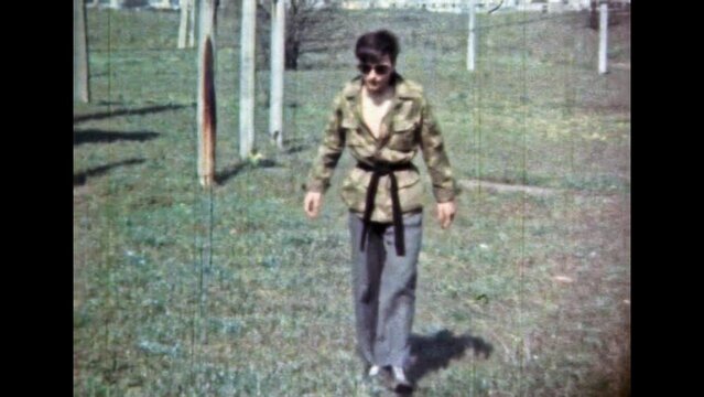 European man karateka smoking on green nature background. Cool man in black glasses, karate fighter sportswear walking outdoors. Courageous handsome person. Vintage color film. Retro 1980s archive