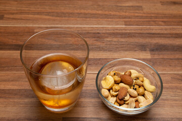 木目テーブルの上の丸い氷のウィスキーオンザロックとおつまみ