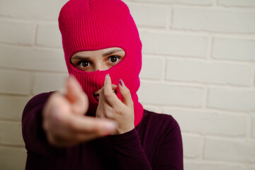 A woman wearing a bright pink balaclava dances energetically, striking unique poses with her hands...