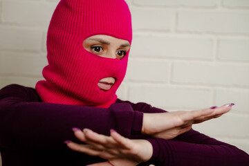 A woman wearing a bright pink balaclava dances energetically, striking unique poses with her hands...