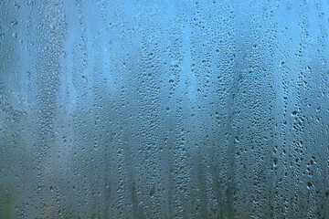 Abstract view with rain droplets on window glass on gloomy autumn day on blur blue background close...