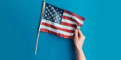 A hand holding a small American flag against a blue background, symbolizing patriotism, national pride, and celebration of American identity