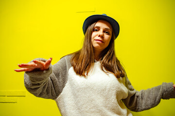 Woman in Cozy Sweater Dancing Against Bright Yellow Wall During Daytime