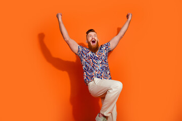 Photo of funky lucky guy dressed print shirt screaming yeah rising fists isolated orange color...