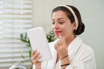 Smiling woman applying red liquid lipstick