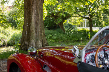Left front of a parked red convertible classic car in a park