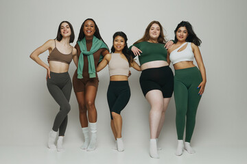 Women of varying shapes, sizes, and ethnicities pose together in comfortable, stylish activewear against neutral background. Concept of beauty and fashion, support, unity, wellness, body positivity.