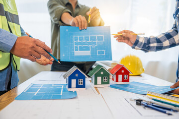 An architect engineer meeting is taking place at a desk covered with blueprints. They are...