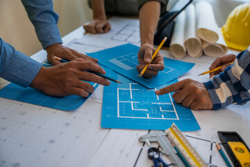 An architect engineer meeting is taking place at a desk covered with blueprints. They are...