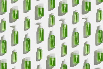 Transparent different plastic bottles with green liquid as trend minimal pattern, skin care, beauty and wellness, body treatment products on light background at sunlight, top view, aesthetic flatly