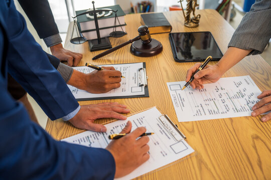 A team meeting of business people and a lawyer in formal suits is taking place at a desk, discussing a contract and various aspects of the law and litigation.