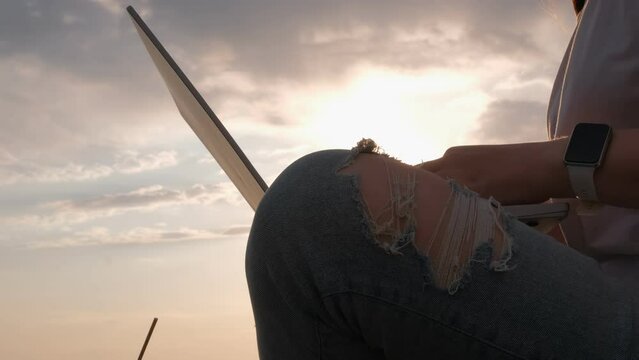 Woman working on laptop outdoors at sunset with jeans and smartwatch in closeup shot
