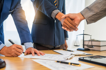 A team meeting of business people and a lawyer in formal suits is taking place at a desk, discussing a contract and various aspects of the law and litigation.