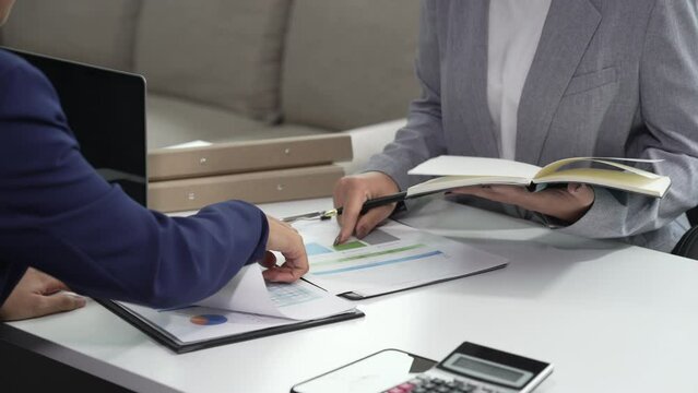 Two Asian businesswomen collaborate on stock market strategies and financial services, exchanging comments and suggestions on loan applications and investment opportunities.