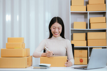 Startup SME small business entrepreneur, young Asian woman, freelancer working at home office, box, smartphone, laptop, online, marketing, packaging, shipping, b2b, SME, ecommerce concept ..