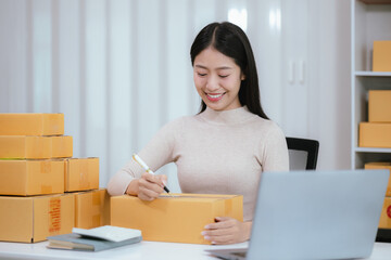 Startup SME small business entrepreneur, young Asian woman, freelancer working at home office, box, smartphone, laptop, online, marketing, packaging, shipping, b2b, SME, ecommerce concept ..