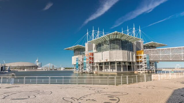 The big Lisbon oceanarium timelapse hyperlapse (aka Oceanario de Lisboa) building on pier in an artificial lagoon at Tagus river estuary in parque das nacoes on sunny day with blue cloudy sky