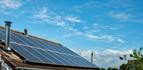 Panoramic image of Solar panels on a domestic house roof with blue sky behind. A sustainable energy image. Good copy space.