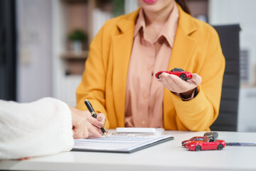 Fototapeta premium Asian businesswoman and a salesman discuss car sales, insurance, and financing with a customer at a desk, covering used car loans, premiums, deductibles, and various insurance coverage options.