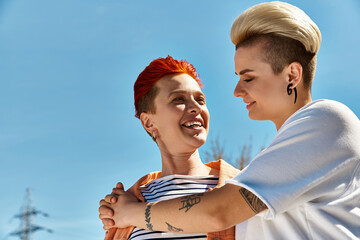 A young lesbian couple proudly standing side by side with a rainbow flag, celebrating love and...
