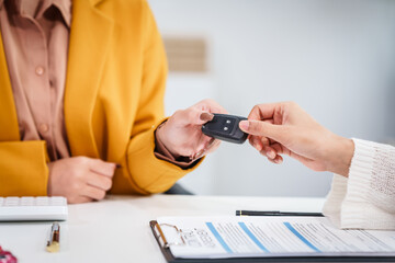 Asian businesswoman hands car keys to a customer while a salesman discusses car sales, insurance,...