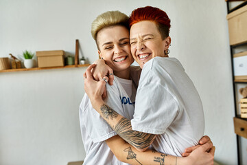 Young women in volunteer t-shirts embrace in a warm hug as they work together for a charitable...