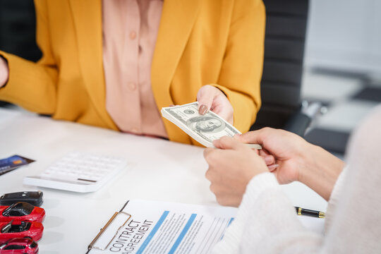 Asian businesswoman hands car keys to a customer while a salesman discusses car sales, insurance, used car loans, and finance options at a desk, covering premiums and coverage types.