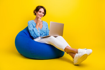 Full length photo of smart girl dressed print blouse sit on pouf look at laptop planing work week...
