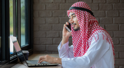 A handsome young Arab businessman in a traditional headdress is talking on the phone.