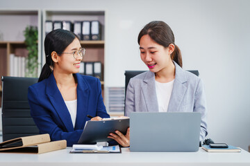 Obraz premium Two Asian businesswomen collaborate on stock market strategies and financial services, exchanging comments and suggestions on loan applications and investment opportunities.