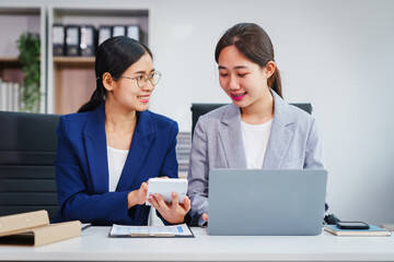 Two Asian businesswomen collaborate on stock market strategies and financial services, exchanging...