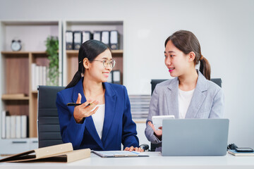 Two Asian businesswomen collaborate on stock market strategies and financial services, exchanging...