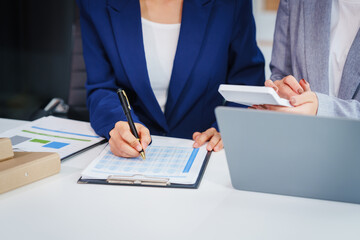 Two Asian businesswomen collaborate on stock market strategies and financial services, exchanging...
