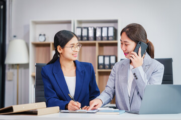 Two Asian businesswomen collaborate on stock market strategies and financial services, exchanging...