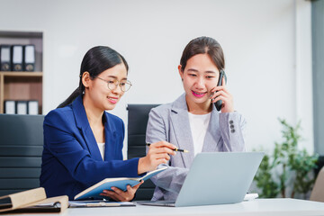 Two Asian businesswomen collaborate on stock market strategies and financial services, exchanging...