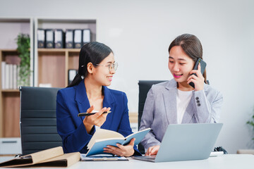 Two Asian businesswomen collaborate on stock market strategies and financial services, exchanging...