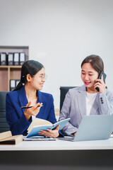 Two Asian businesswomen collaborate on stock market strategies and financial services, exchanging...