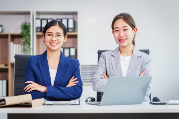 Two Asian businesswomen collaborate on stock market strategies and financial services, exchanging...