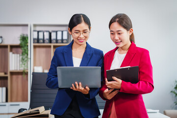 Two Asian businesswomen collaborate on stock market strategies and financial services, exchanging...