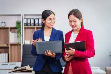 Two Asian businesswomen collaborate on stock market strategies and financial services, exchanging...