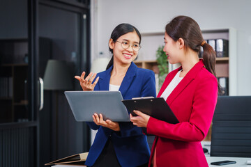 Two Asian businesswomen collaborate on stock market strategies and financial services, exchanging...