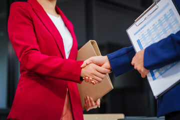 Two Asian businesswomen shake hands, collaborating on financial matters, discussing comments and...
