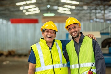 Two happy factory workers wearing hard hats and safety vests standing with arms crossed.