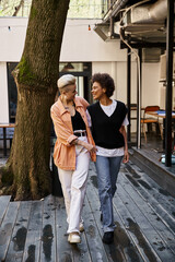 Two women peacefully walk next to a tree on a wooden walkway.