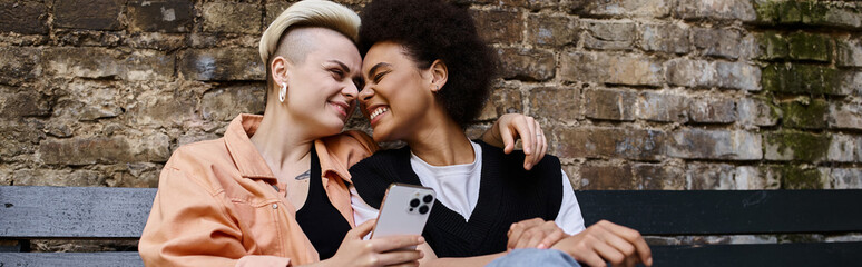 A diverse couple of women sit peacefully on a wooden bench.