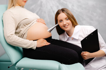 A gynecologist leans a stethoscope to a pregnant woman's belly and listens to the baby's heartbeat