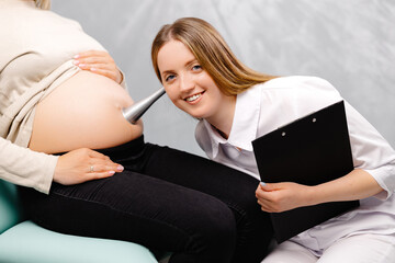 A gynecologist leans a stethoscope to a pregnant woman's belly and listens to the baby's heartbeat