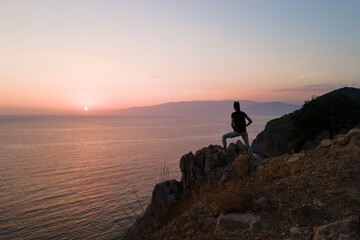 Female hiker on rocky shore with beautiful seascape at sunset, aerial orbital shot