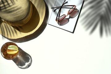 Summer vacation flat lay, white background - straw sun hat sunglasses on book with drink palm shadows